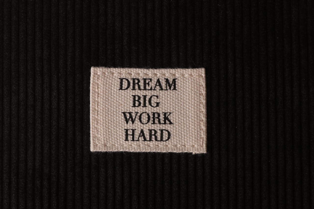 about-03 Close-up of patch with 'Dream Big, Work Hard' text on textured black fabric.